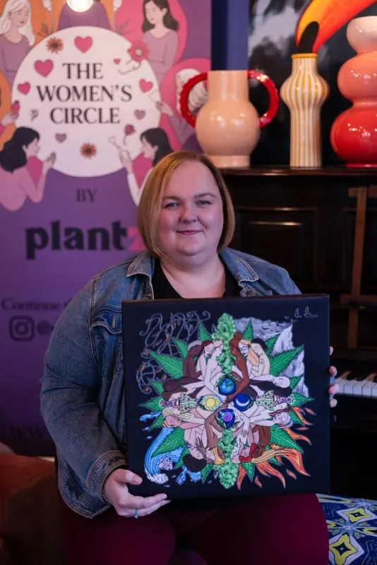 A Women's Circle guest holding up a colourful piece of artwork celebrating women and plant medicine