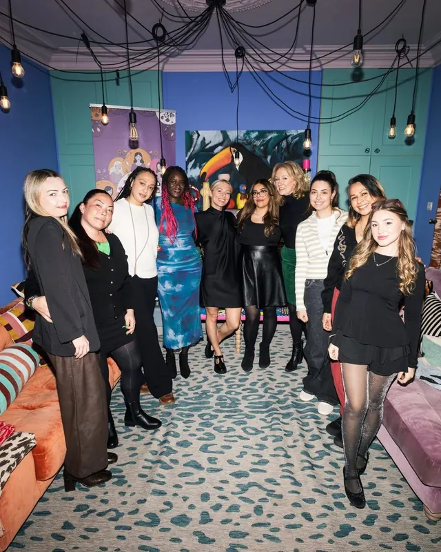 A large group of Women's Circle guests posing together in a colourful lounge decorated with hanging bulb lights