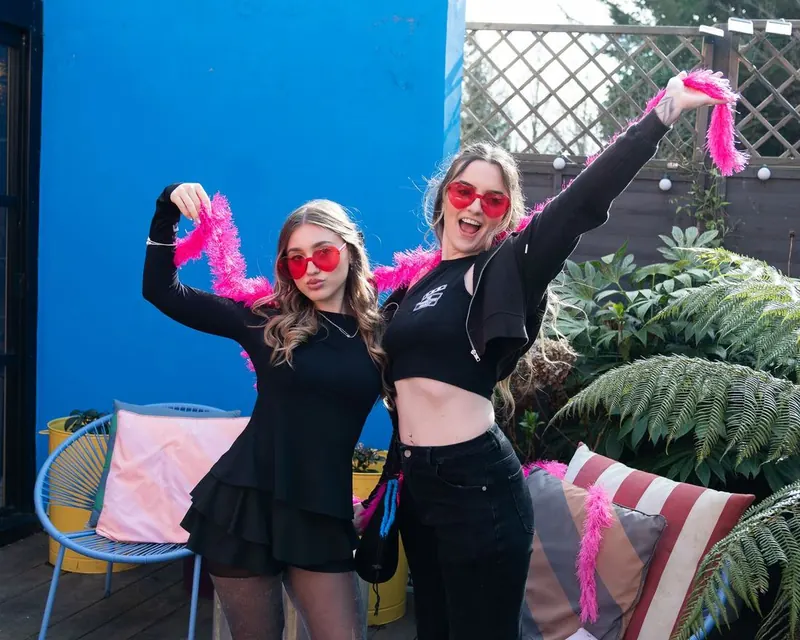 Two Women's Circle guests on a terrace with pink feather boas
