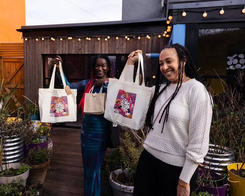 Two Women's Circle guests holding up branded Women's Circle tote bags outdoors