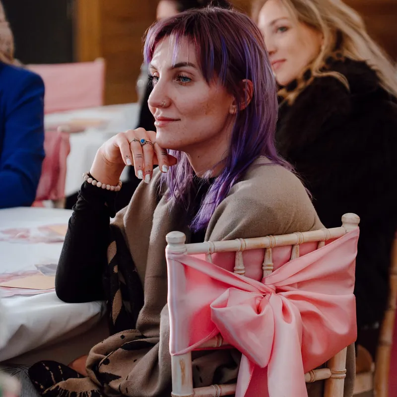 A woman with purple hair smiling as she listens to a talk at Circle 2.0