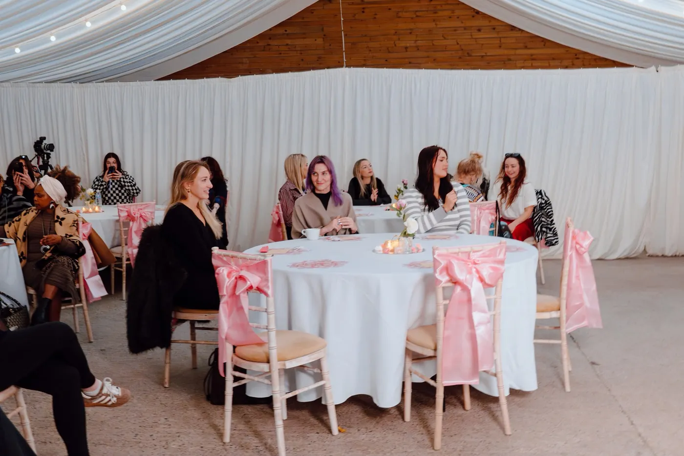 Women gathered around tables dressed with pink bows, listening at Circle 2.0, The Cycle Edition